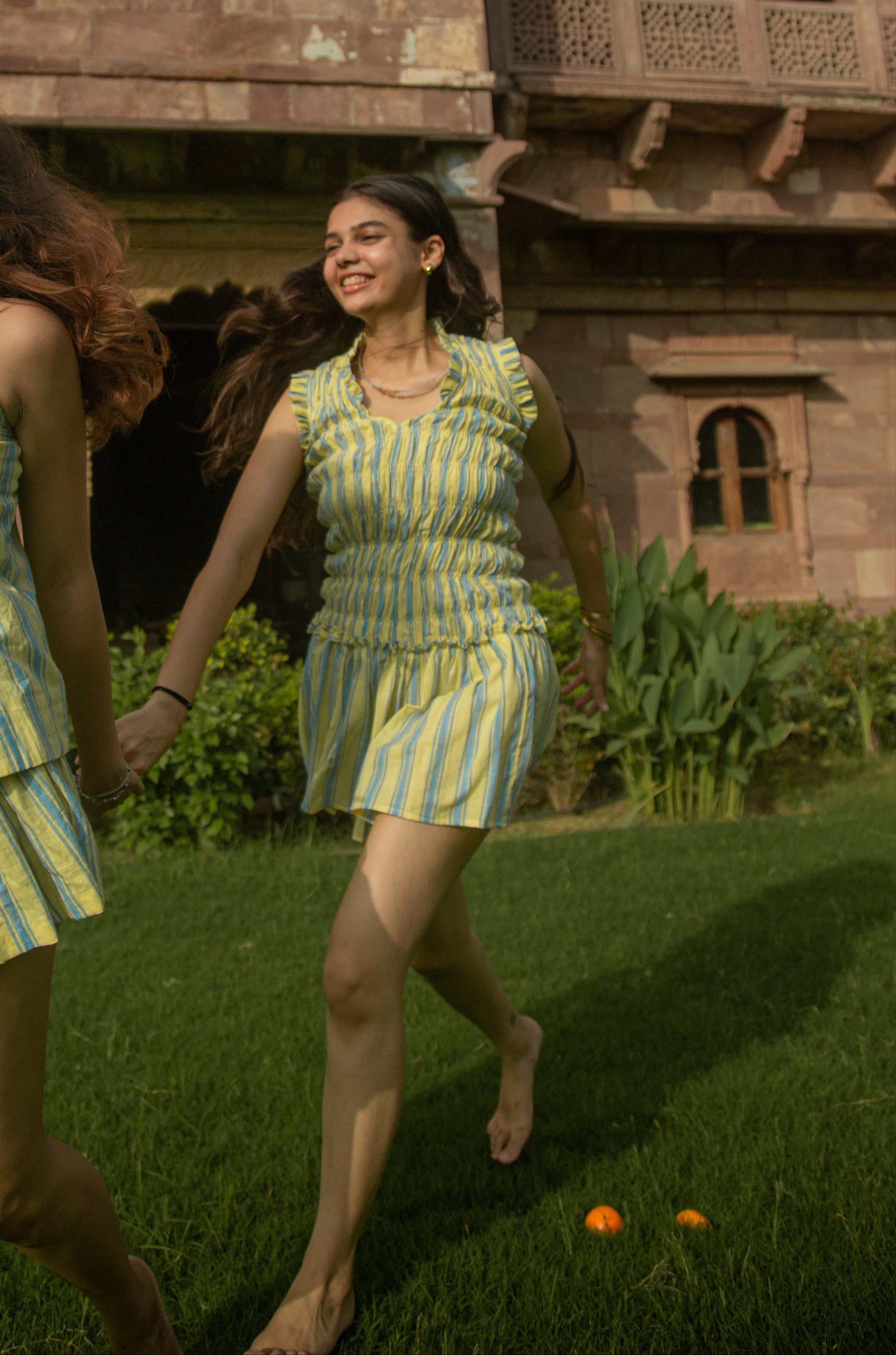 Two women in matching yellow and green outfits walking in front of a traditional building.